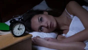Woman in her 40s experiencing perimenopause insomnia, lying awake in bed with a worried expression