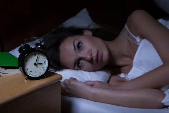 Woman in her 40s experiencing perimenopause insomnia, lying awake in bed with a worried expression
